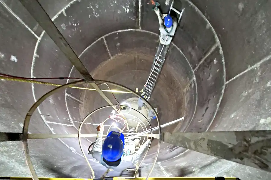 Técnicos con casco, arnés y línea de vida realizando mantenimiento dentro de un silo de almacenamiento de alimentos